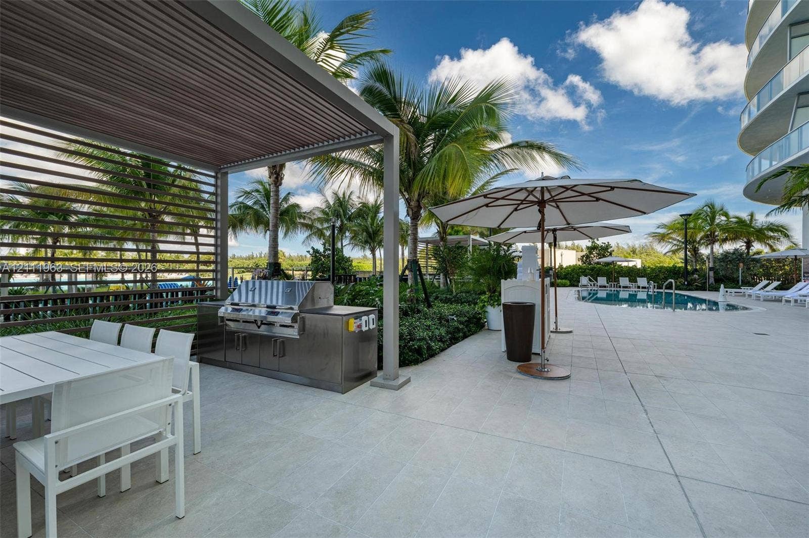 Outdoor kitchen station featuring a stainless steel built-in grill, dark stone countertop, and sleek metallic cabinetry set within a screened pavilion