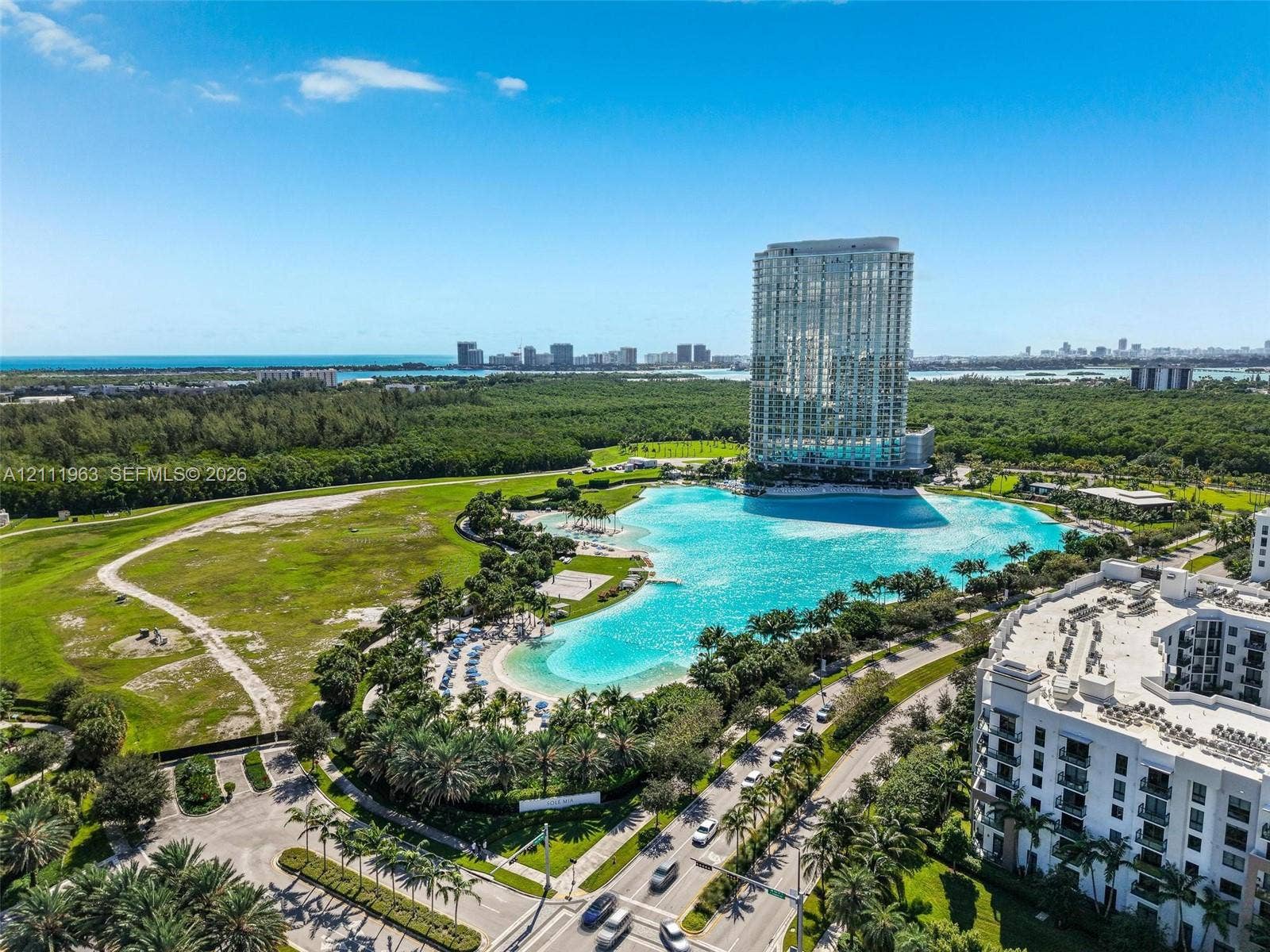 Aerial perspective featuring a large crystalline lagoon, coastal skyline, and dense woodland surroundings