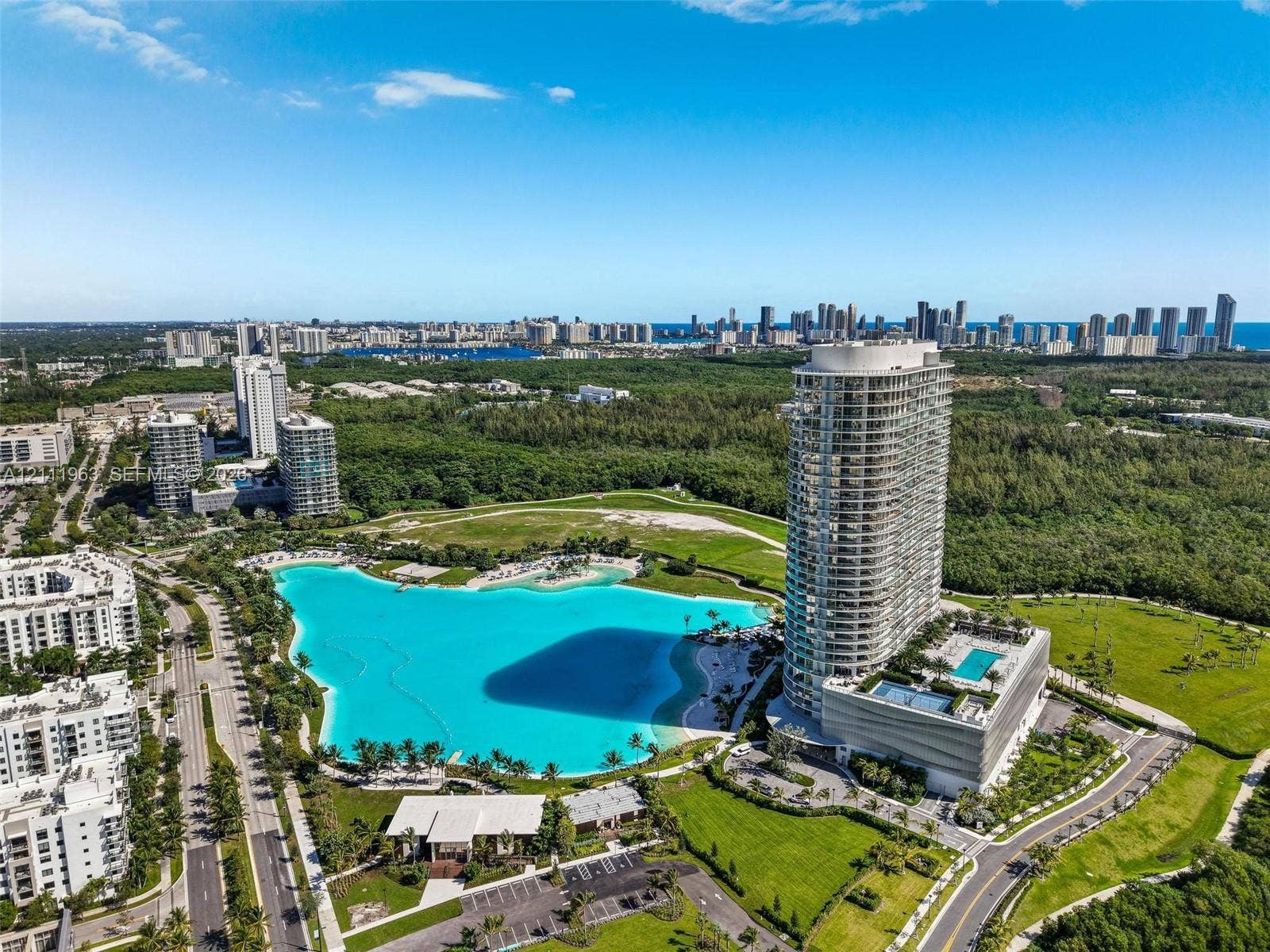 High-rise residential exterior featuring expansive wrap-around balconies, a large swimming pool, a dedicated tennis court, and manicured landscaping with mature palm trees