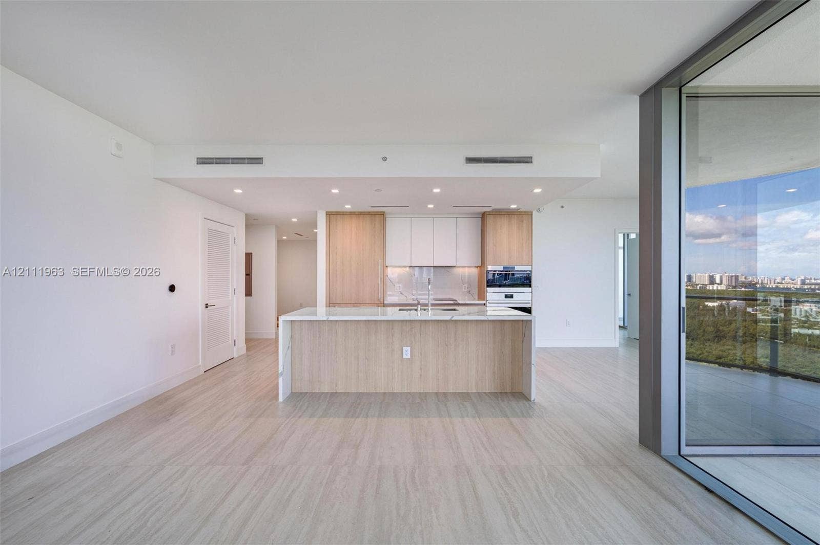 Floor-to-ceiling glass sliding doors, private balcony, neutral large-format tile flooring, and coastal landscape