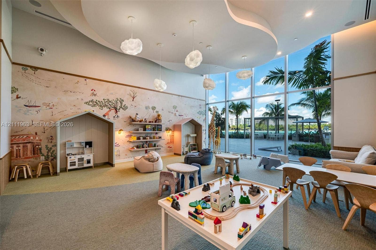 High-ceilinged room featuring a sculpted tray ceiling with pendant lighting, custom built-in cabinetry with integrated shelving, house-shaped architectural wall alcoves, and a decorative mural wall