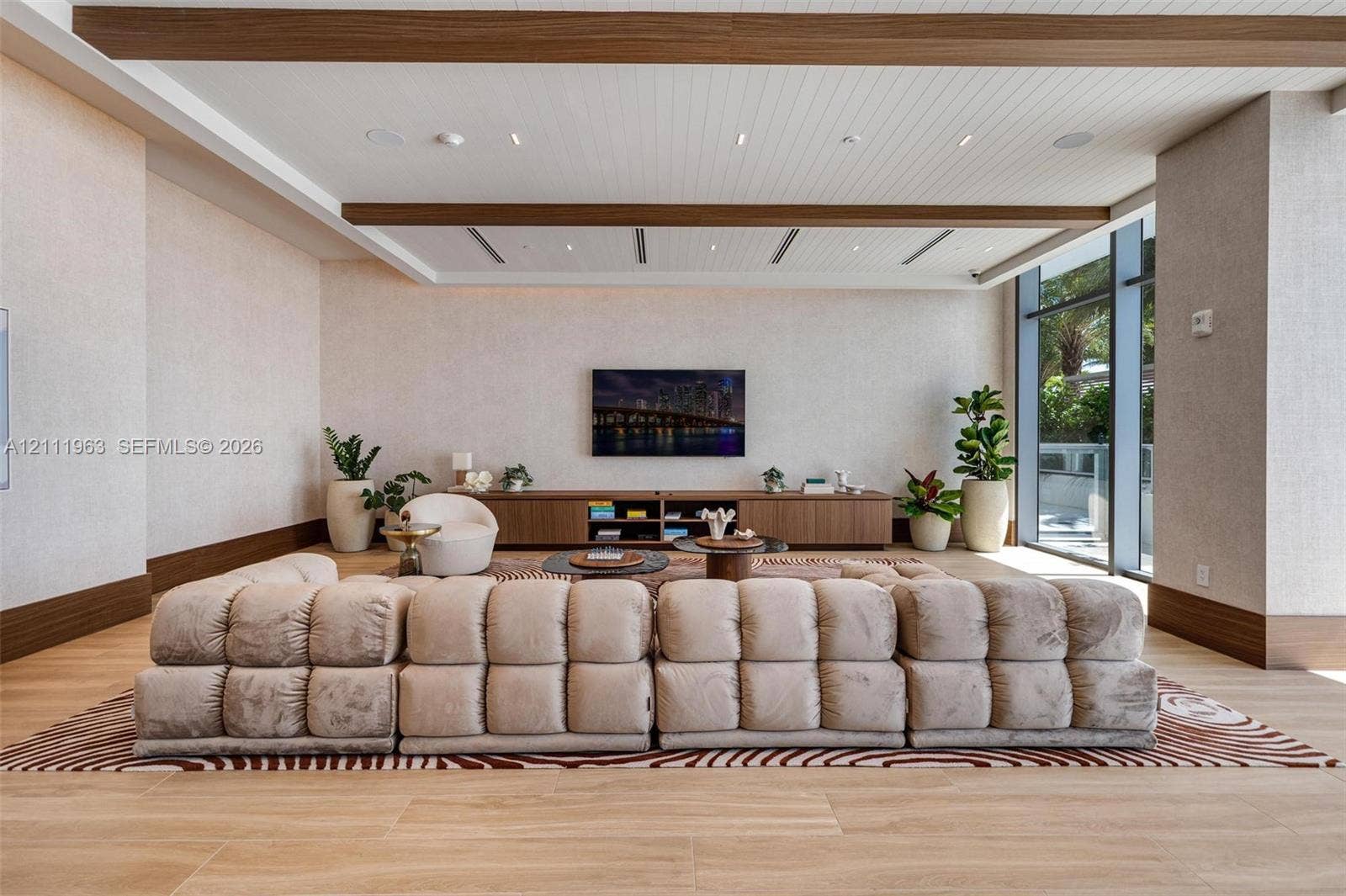 Floor-to-ceiling glass panel doors, wood-finish plank flooring, ceiling with exposed decorative beams, integrated recessed lighting, and built-in bar cabinetry with stone-surface counters