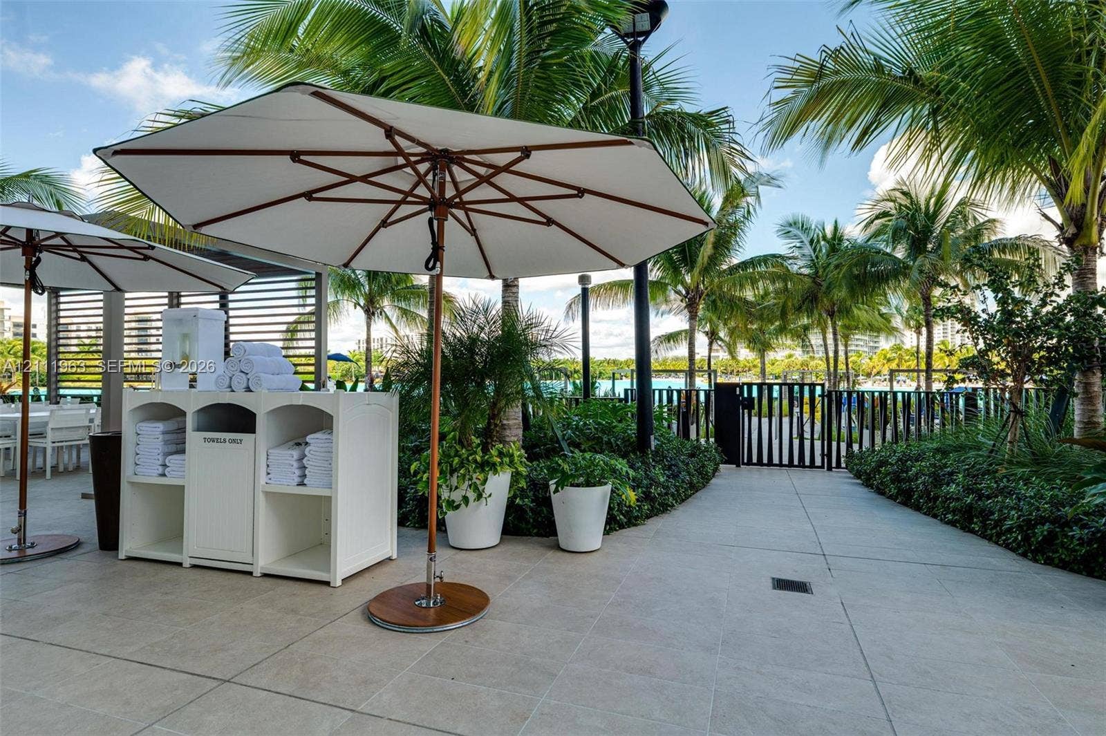 Outdoor space featuring a gray hard-sided spa, minimalist pergola structure, stone-finish paving, and mature perimeter landscaping