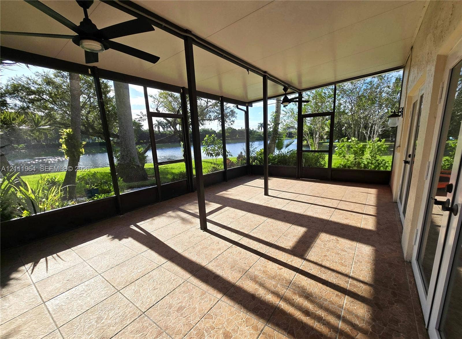 Screened-in lanai featuring tile flooring, a solid roof structure, ceiling fans, and a water frontage