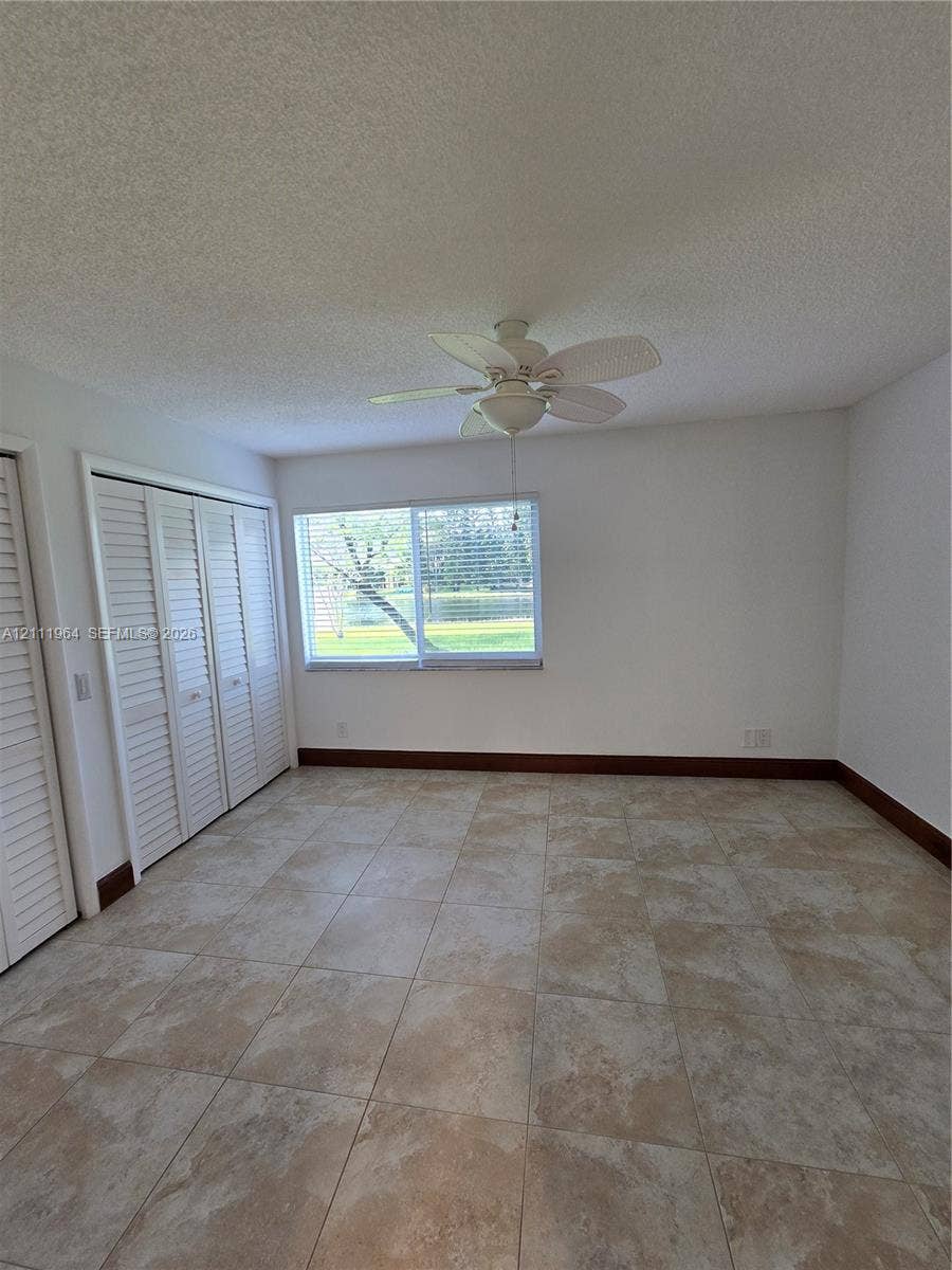 Room featuring tile flooring, ceiling fan, and louvered double-closet doors
