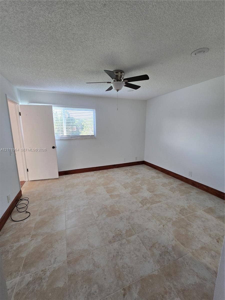 Neutral-toned tile flooring, dark wood-finished trim, ceiling-mounted fan, and horizontal window blinds