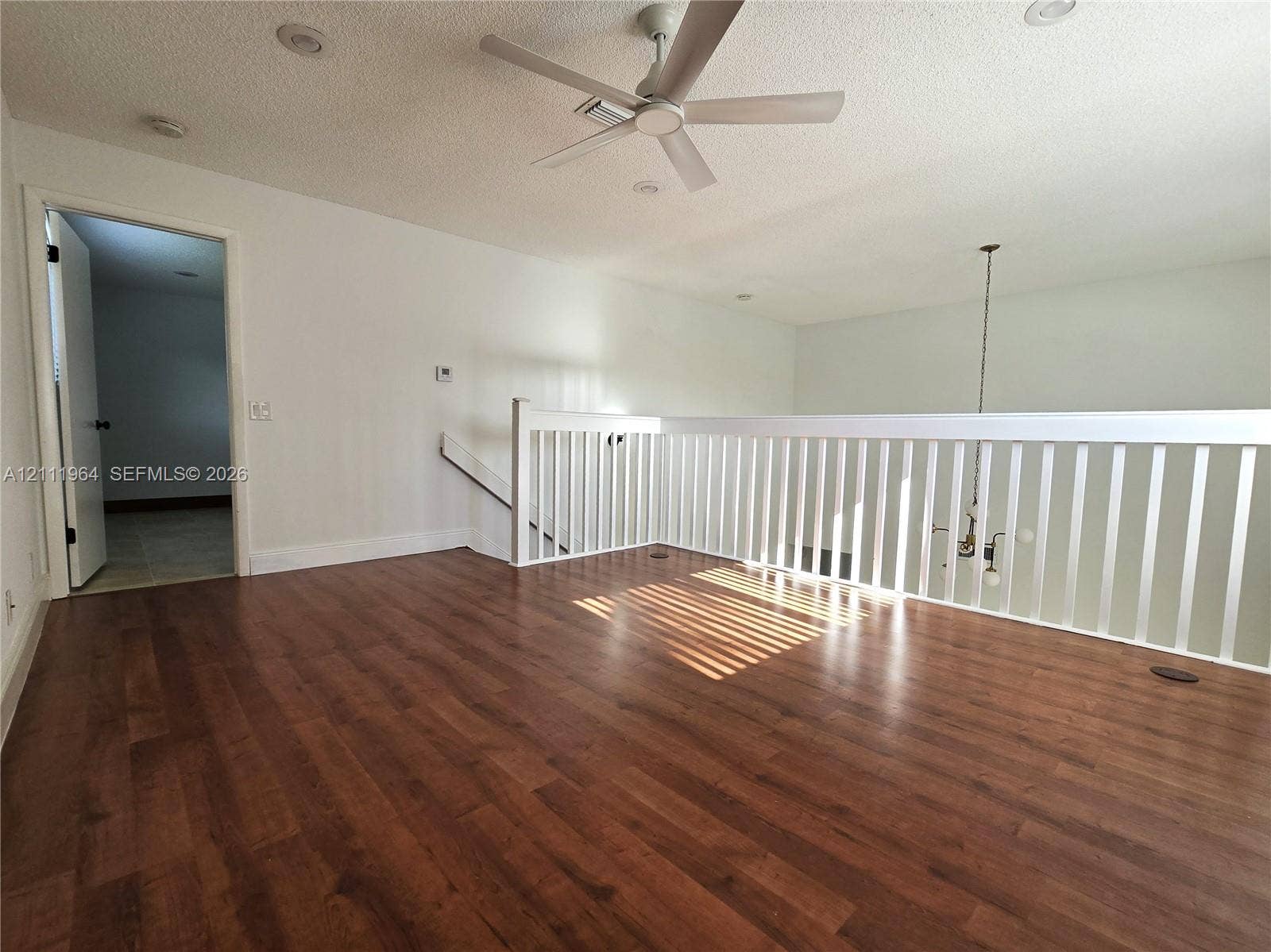 Wood-finish flooring, white spindle railing, ceiling fan, recessed lighting, and a pendant light fixture