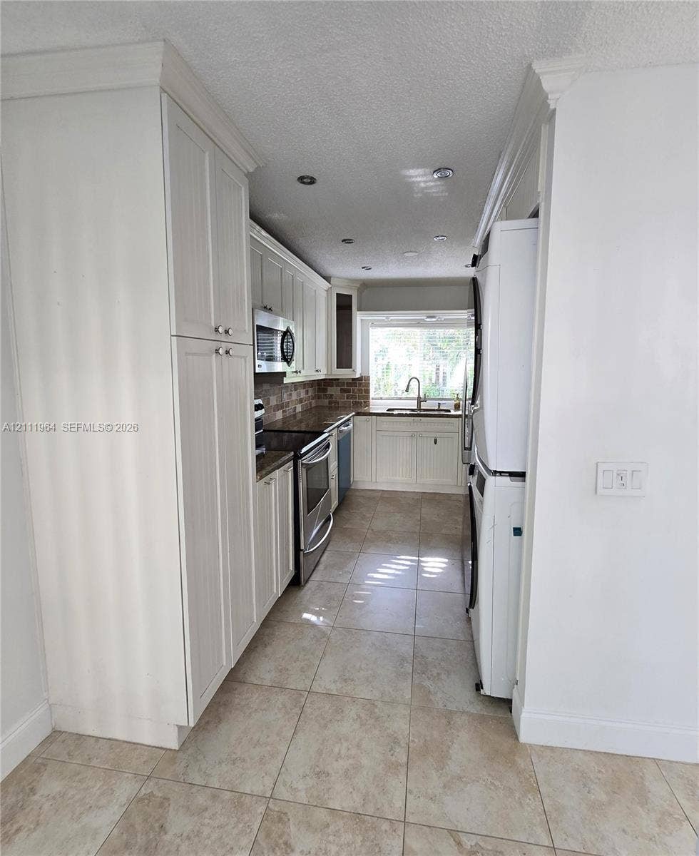 Kitchen featuring white shaker-style cabinetry, stainless steel appliances, tiled backsplash, stone-finish floor tile, and recessed lighting