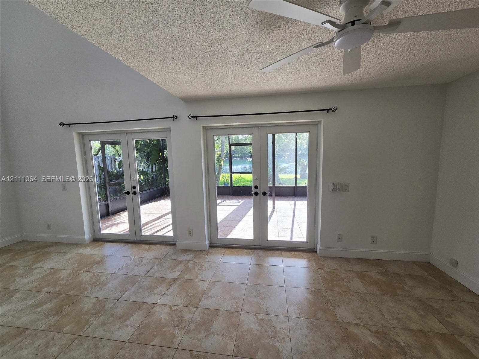 Vaulted ceilings featuring a white finish, neutral-toned tile flooring, dual sets of glass-paned double doors, and a ceiling-mounted light fixture with a fan