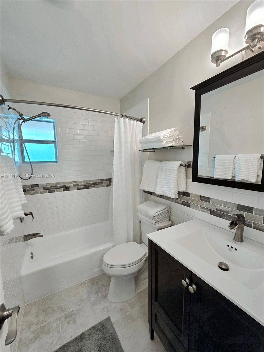 5387 SW 40th Avenue, #203, Dania Beach, FL 33314 Dark-finish vanity with an integrated white sink, wall-mounted light fixture, decorative glass and stone mosaic backsplash, and shower-tub combination with white subway tile