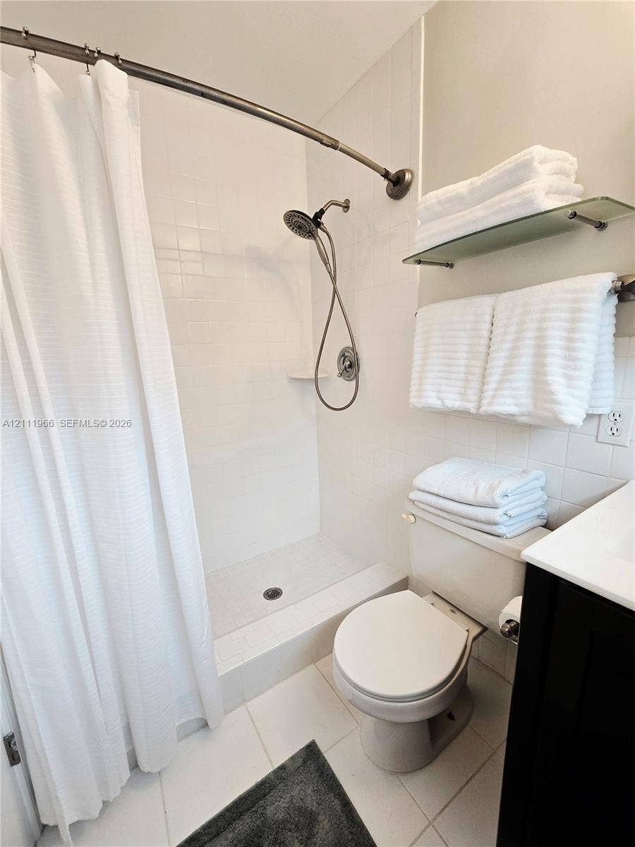 5387 SW 40th Avenue, #203, Dania Beach, FL 33314 Shower enclosure featuring white wall tile, a handheld shower fixture, built-in soap niche, and a wall-mounted glass shelf