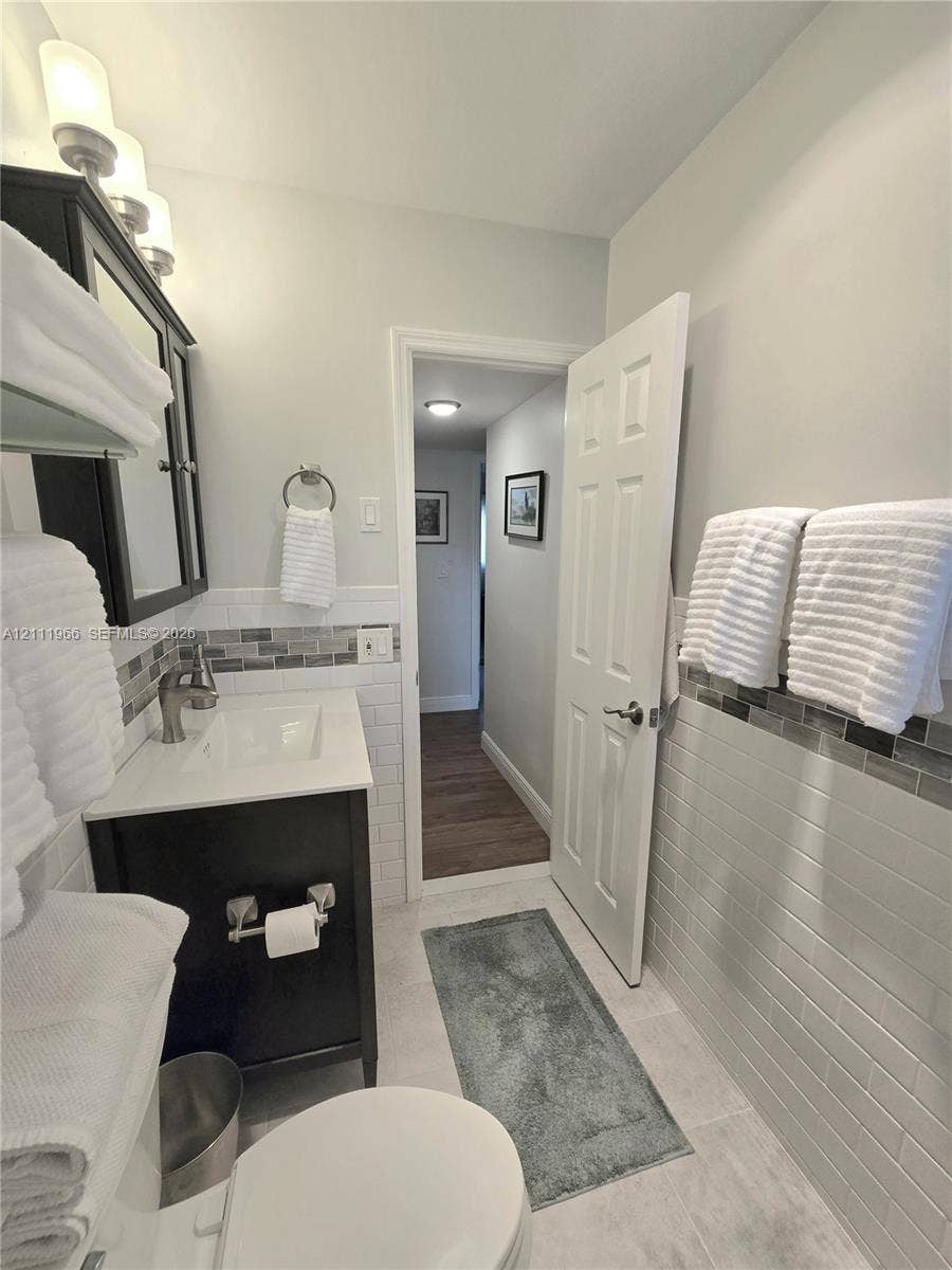 5387 SW 40th Avenue, #203, Dania Beach, FL 33314 Bathroom featuring a dark wood-finish vanity with a white rectangular sink, white subway tile walls with horizontal glass tile accents, and a six-panel door