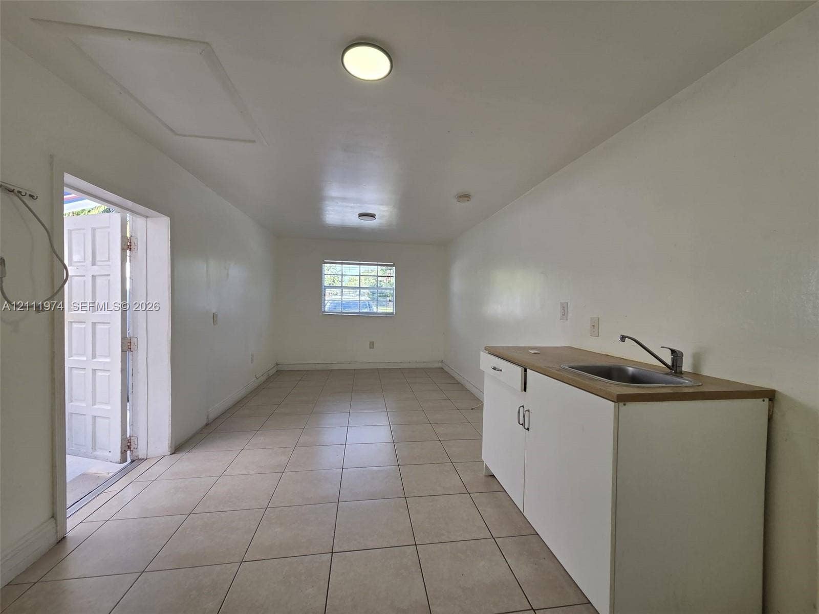600 SW 44th Court, Miami, Miami, FL 33134 Interior space featuring neutral ceramic tile flooring, built-in cabinetry with a countertop, stainless steel sink with a goose-neck faucet, and exterior access via a multi-panel door