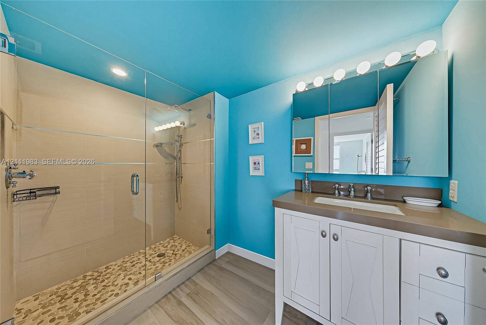 90 Alton Road, #TH-8, Miami Beach, FL 33139 Walk-in shower with a glass enclosure, pebble-tile flooring, and built-in shelving, complemented by a white vanity with an integrated sink, stone-finish countertop, and a mirrored medicine cabinet