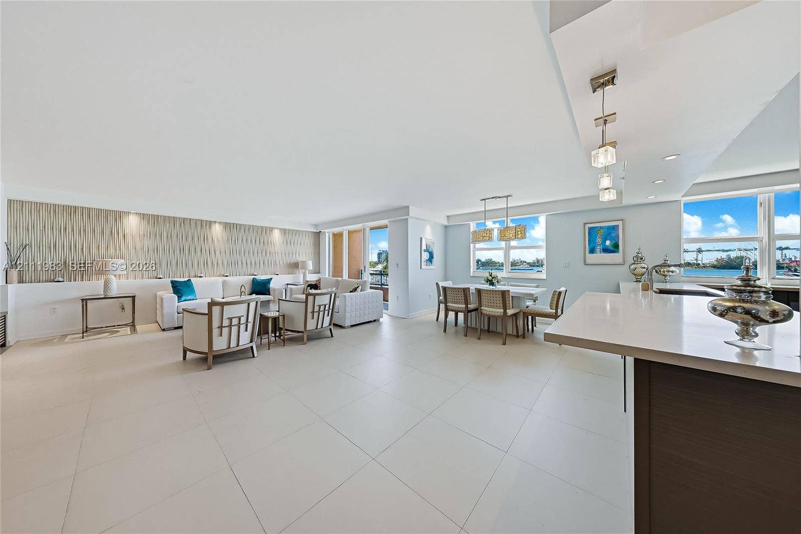 90 Alton Road, #TH-8, Miami Beach, FL 33139 Open-concept interior featuring large-format tile flooring, a stone-surfaced island, textured feature wall with recessed lighting, and expansive windows