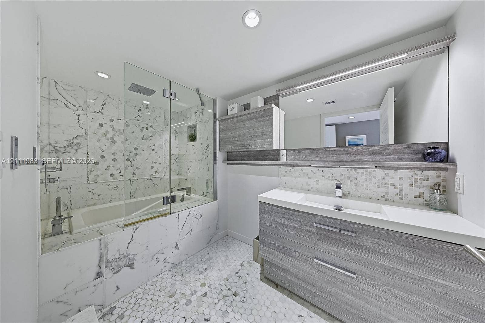 90 Alton Road, #TH-8, Miami Beach, FL 33139 Bathroom featuring a wood-finish floating vanity with an integrated sink, a glass-enclosed soaking tub with stone-tiling, a wall-to-wall mirror, and hexagonal tile flooring