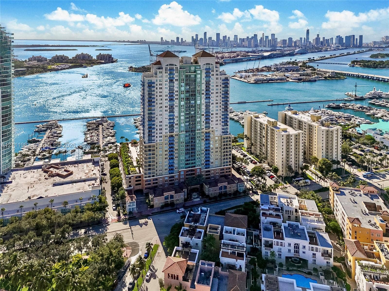 90 Alton Road, #TH-8, Miami Beach, FL 33139 High-rise waterfront building featuring an expansive terrace deck, prominent architectural balconies, and proximity to a marina, set against a coastal skyline backdrop