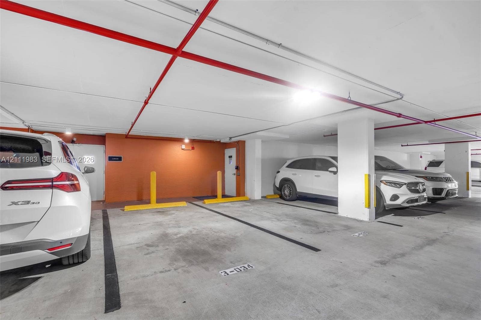 90 Alton Road, #TH-8, Miami Beach, FL 33139 Covered parking garage featuring concrete flooring, structural support pillars, assigned space markers, and high-visibility wheel stops