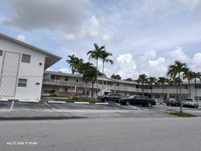 Multi-story exterior featuring white stucco cladding, decorative latticework, second-level railed walkways, and landscaped palm trees