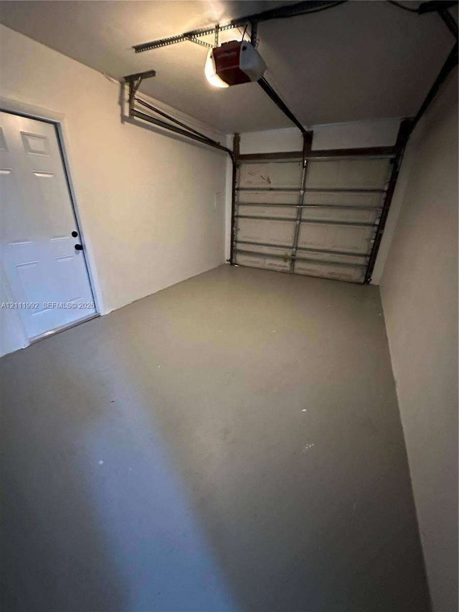 Garage interior featuring a painted concrete floor, neutral wall finish, sectional overhead door, and a dedicated pedestrian side door