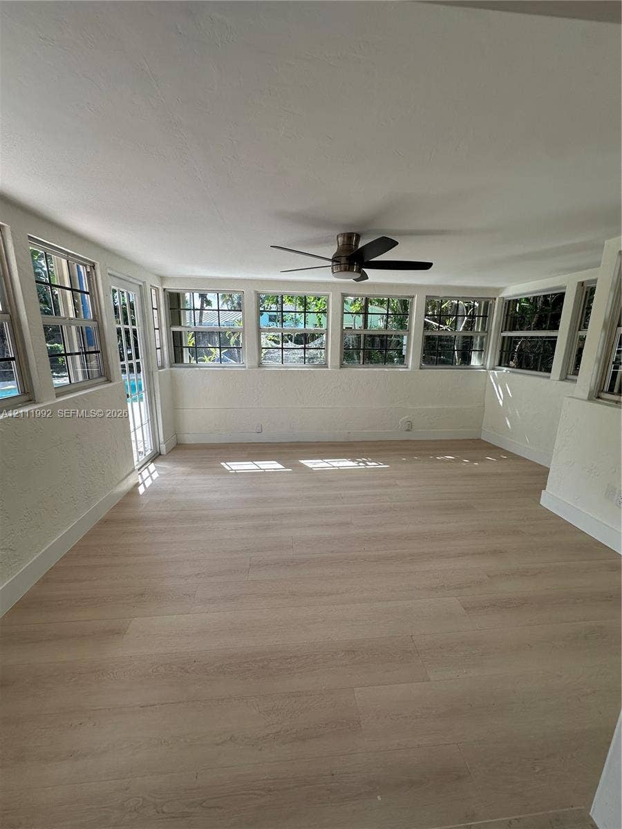Sunroom featuring wood-finish flooring, a series of multi-pane windows, and an overhead ceiling fan