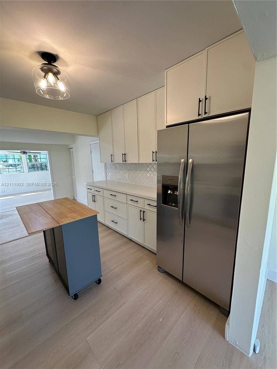 Kitchen featuring white shaker-style cabinetry, matte black hardware, stone-surface countertops, a full-height tile backsplash, and wood-finish flooring
