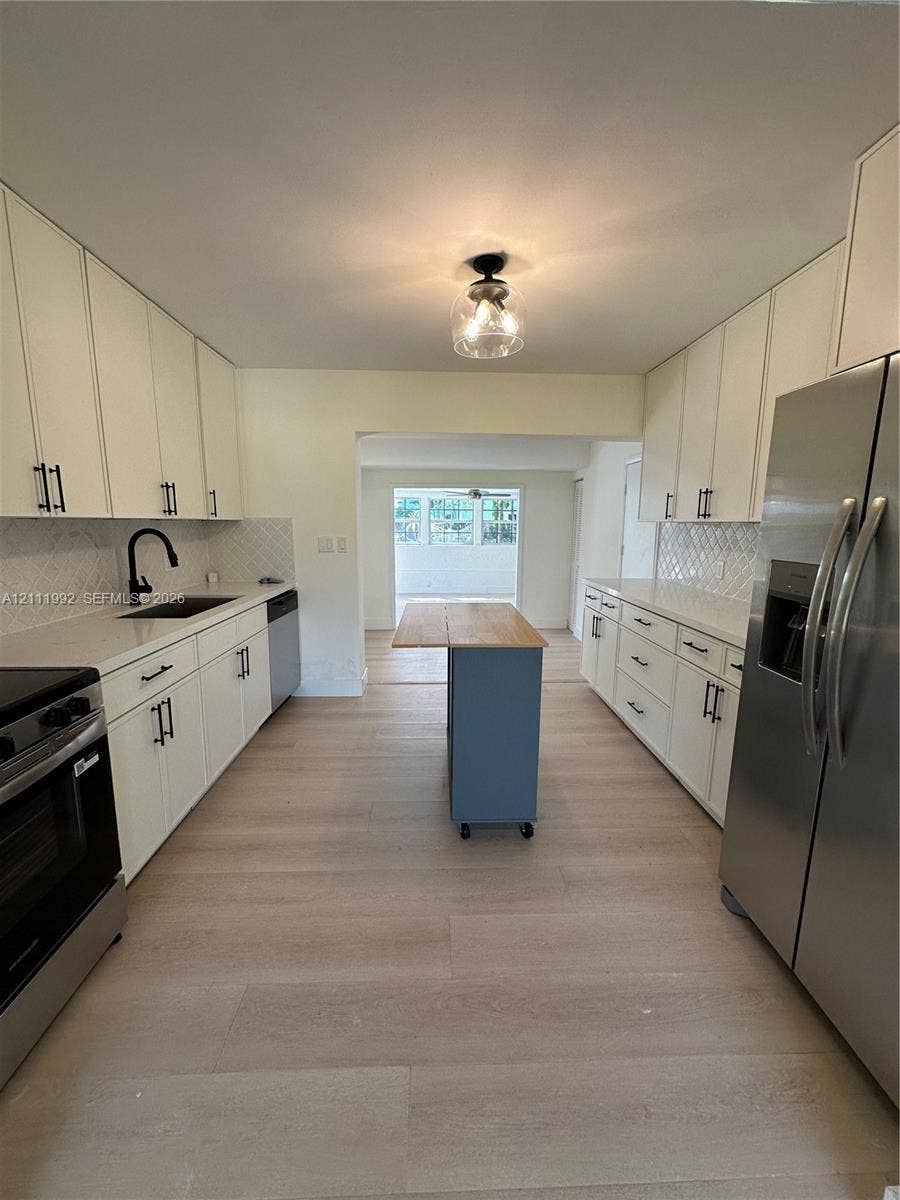 Kitchen featuring white cabinetry with matte black hardware, stone-surface countertops, a diamond-pattern tile backsplash, stainless steel appliances, and wood-finish flooring