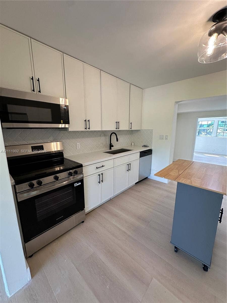 Kitchen featuring white shaker-style cabinetry, stainless steel appliances, white stone-finish countertops, geometric-patterned backsplash, and wood-finish flooring