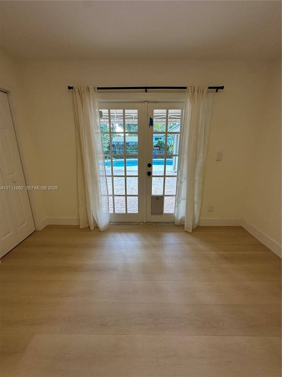 Interior space featuring wood-finish flooring, light-toned walls, and French doors leading to an exterior paved area with a swimming pool