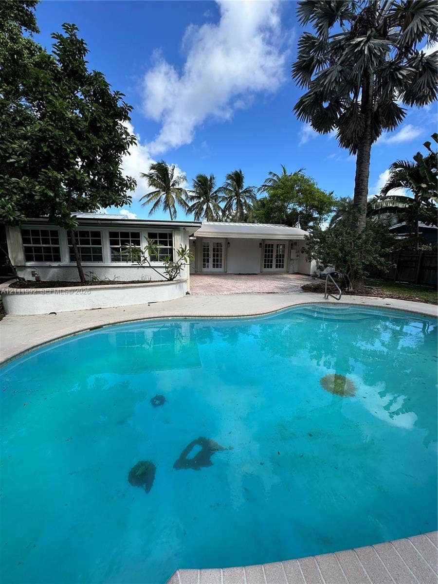In-ground swimming pool with stone-tiled deck, curved concrete retaining wall, and exterior multi-pane windows