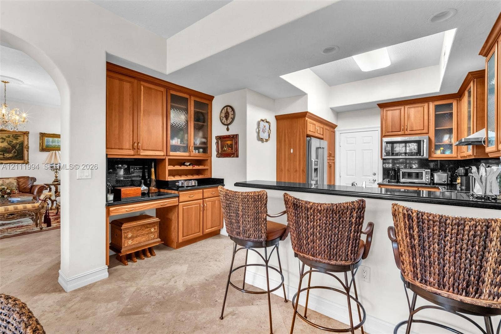 Kitchen featuring custom wood cabinetry, integrated built-in desk area, dark stone countertops, stone flooring, and a tray ceiling with recessed lighting