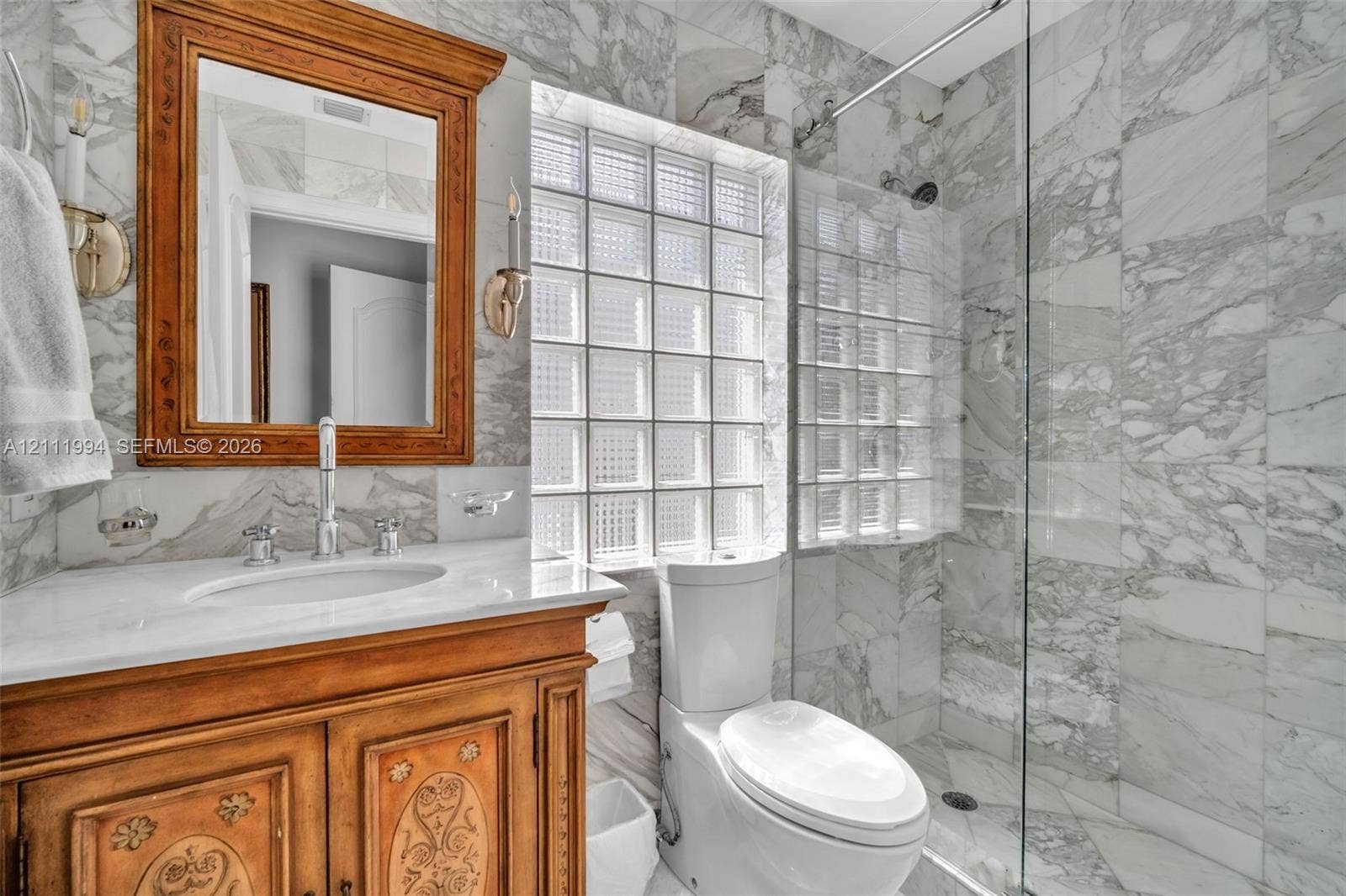 Custom wood vanity with stone countertop, glass block window, floor-to-ceiling stone wall tiling, and glass-enclosed shower