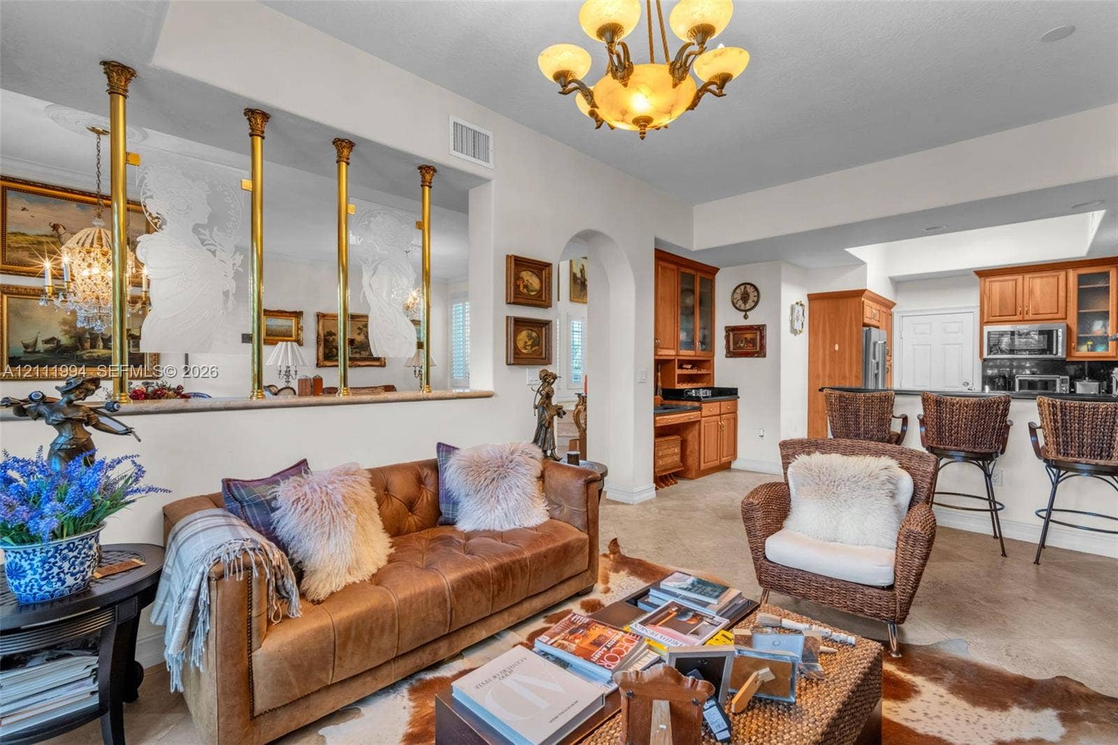 Open-concept interior featuring a half-wall partition with brass columns, tile flooring, built-in cabinetry, and a coffered ceiling with a multi-arm chandelier