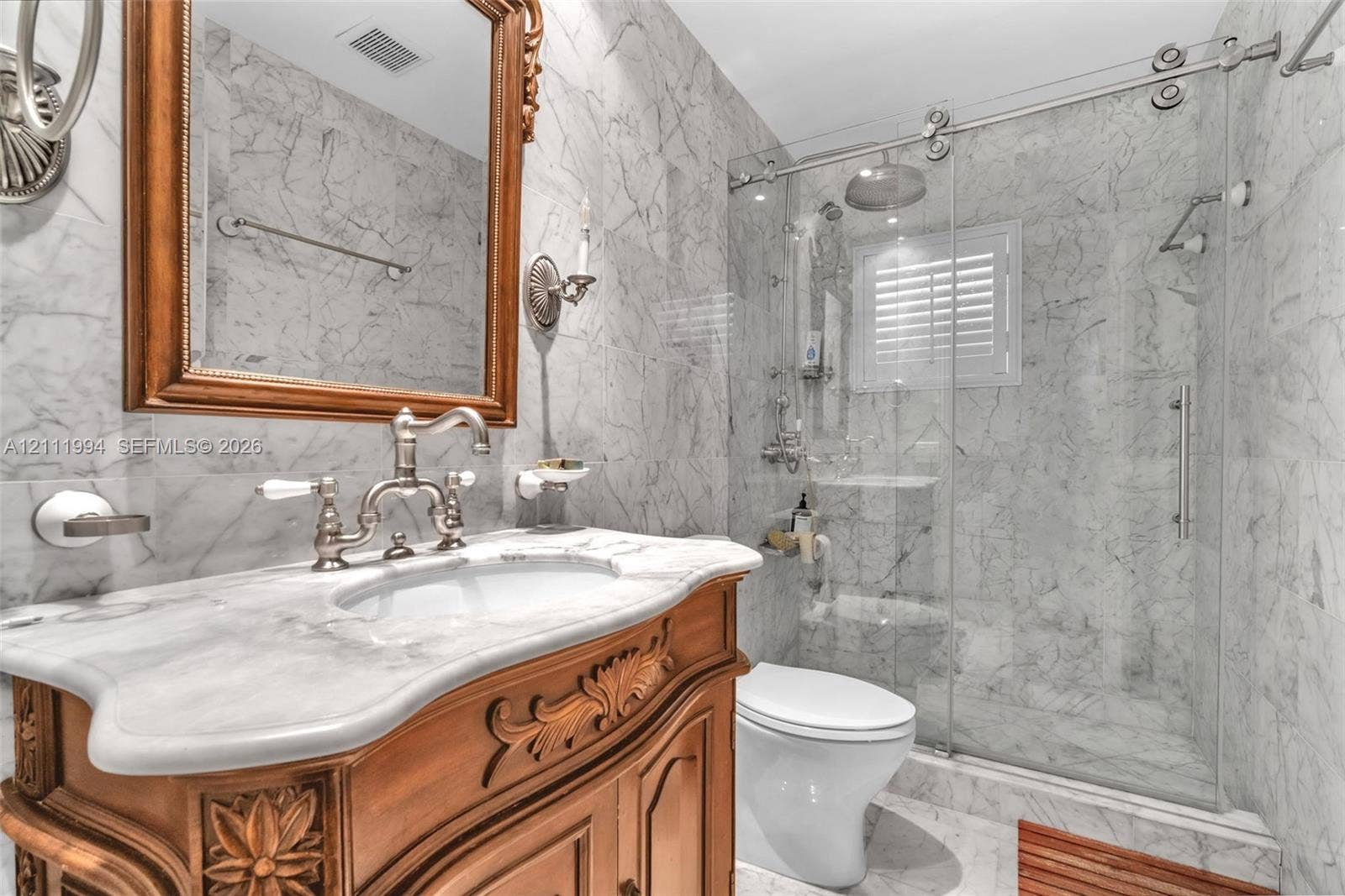Bathroom featuring floor-to-ceiling stone tile, ornate wood-finish vanity with an integrated basin, wall-mounted faucet, and a glass-enclosed shower with a rainfall showerhead