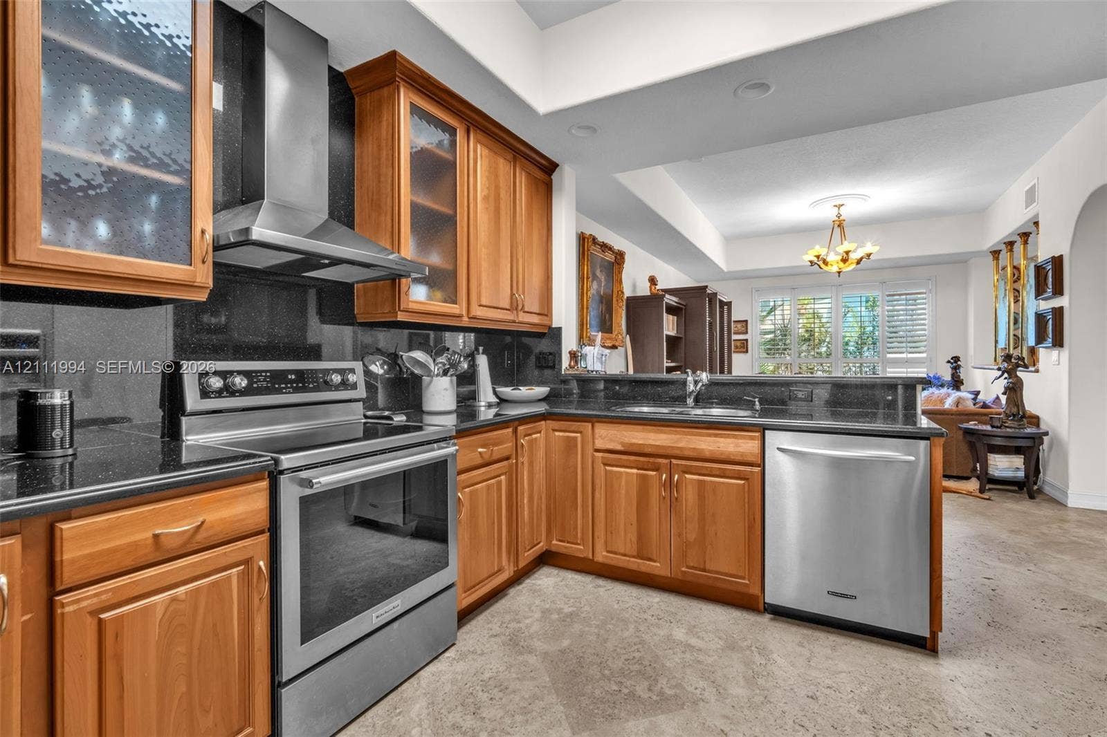 Kitchen featuring stained wood cabinetry with glass-panel upper doors, dark stone-finish countertops, stainless steel appliances, and stone-finish tile flooring