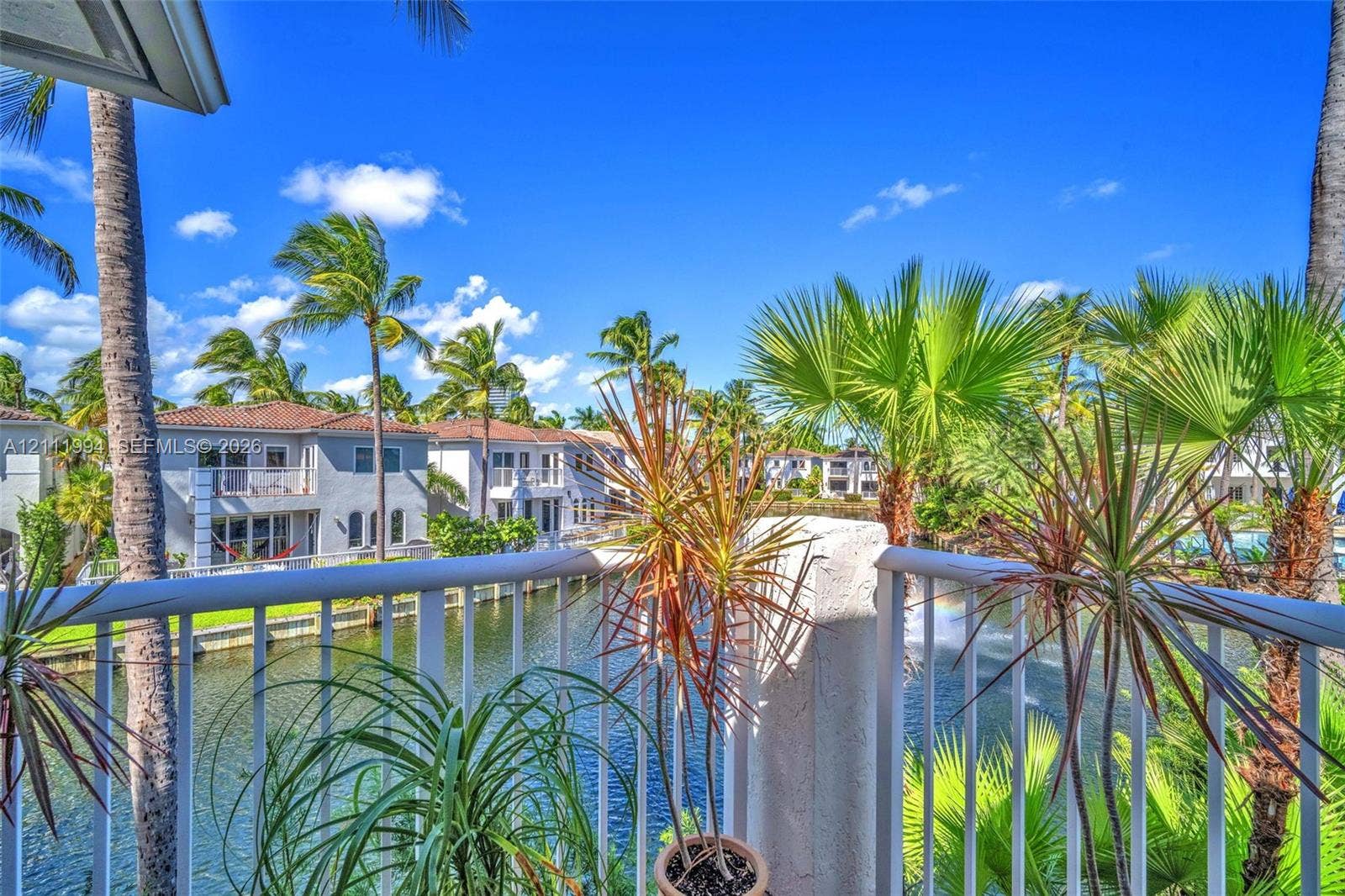 Private balcony with white metal railings overlooking a canal with mature palm trees and lush tropical landscaping