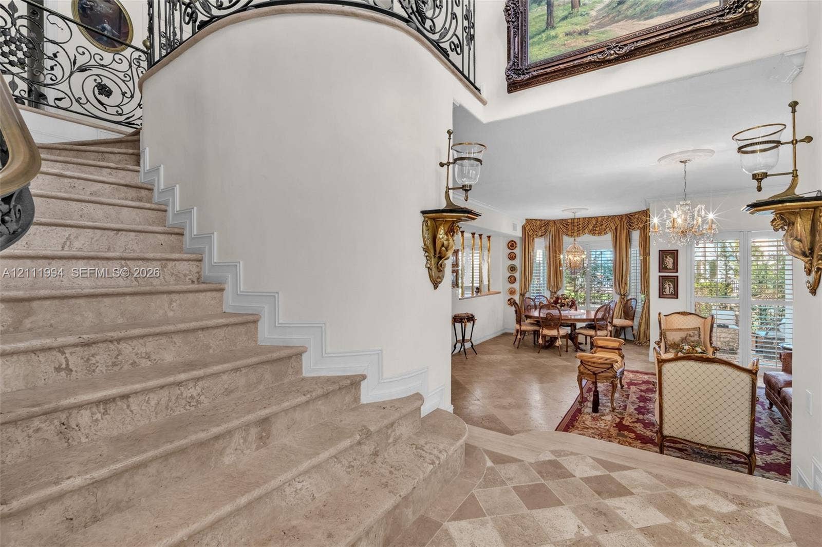 Curved staircase with natural stone treads, intricate wrought-iron railings, stone diamond-patterned flooring, and ornamental wall-mounted light fixtures