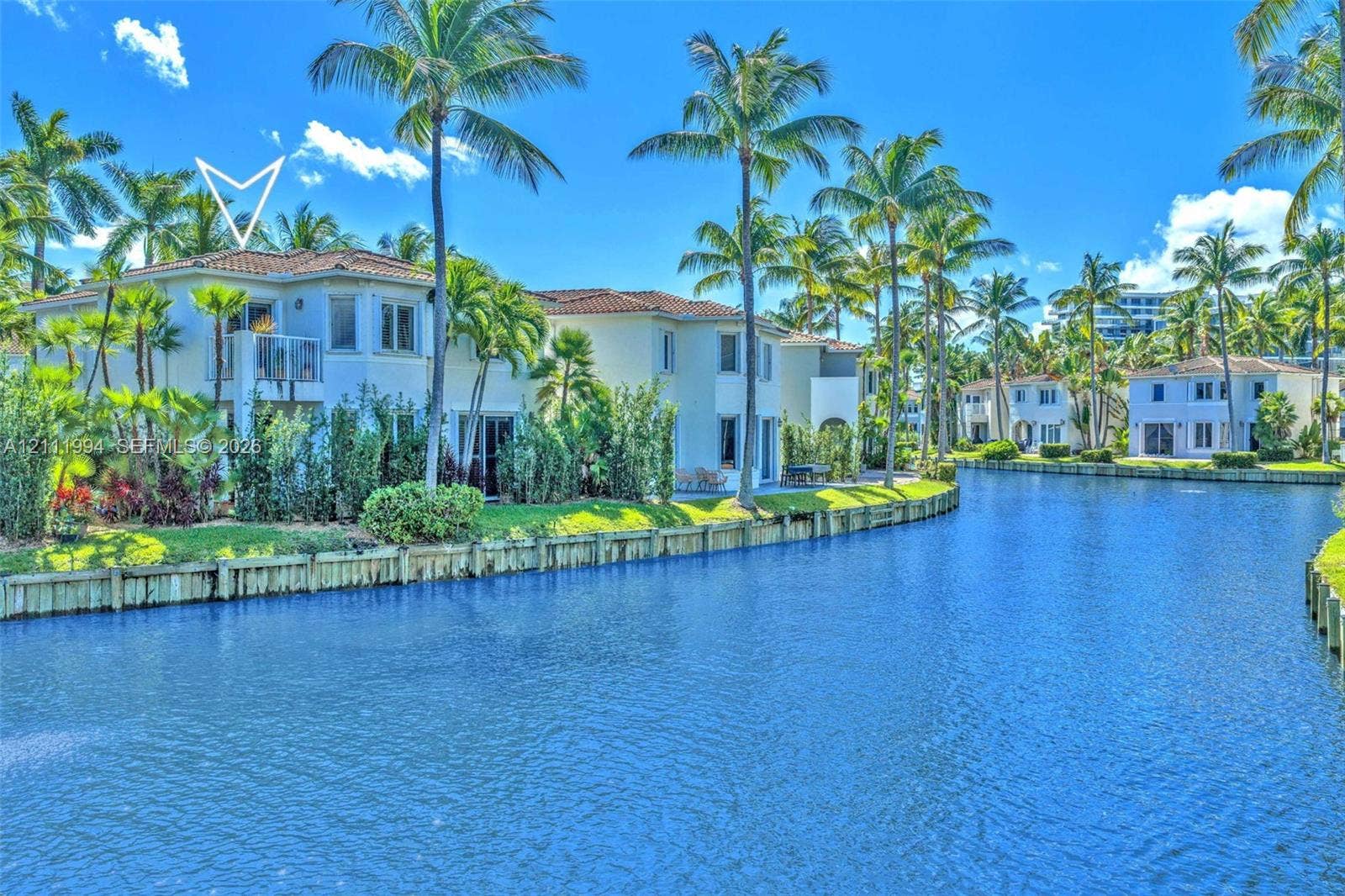 Waterfront exterior featuring a tile roof, second-story balcony, wood bulkhead, and mature landscaping