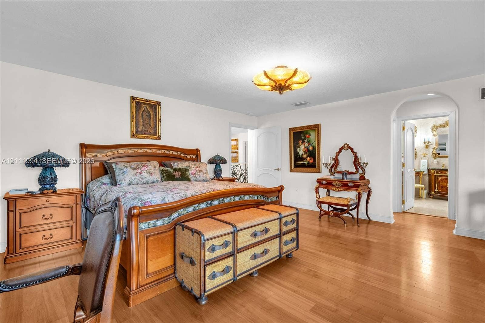 Spacious room featuring wood-finish flooring, a decorative multi-bulb flush mount ceiling fixture, and an arched doorway leading to a secondary room