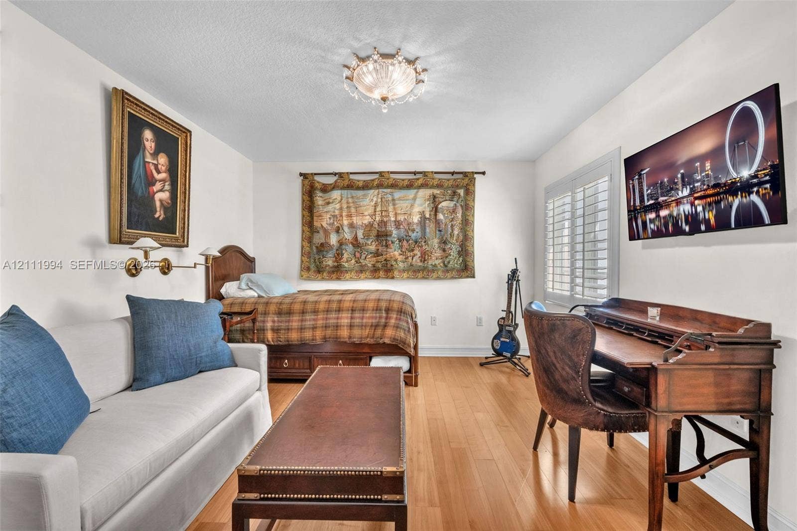 Interior space featuring wood-finish flooring, white walls, plantation shutters, and a decorative flush-mount ceiling fixture