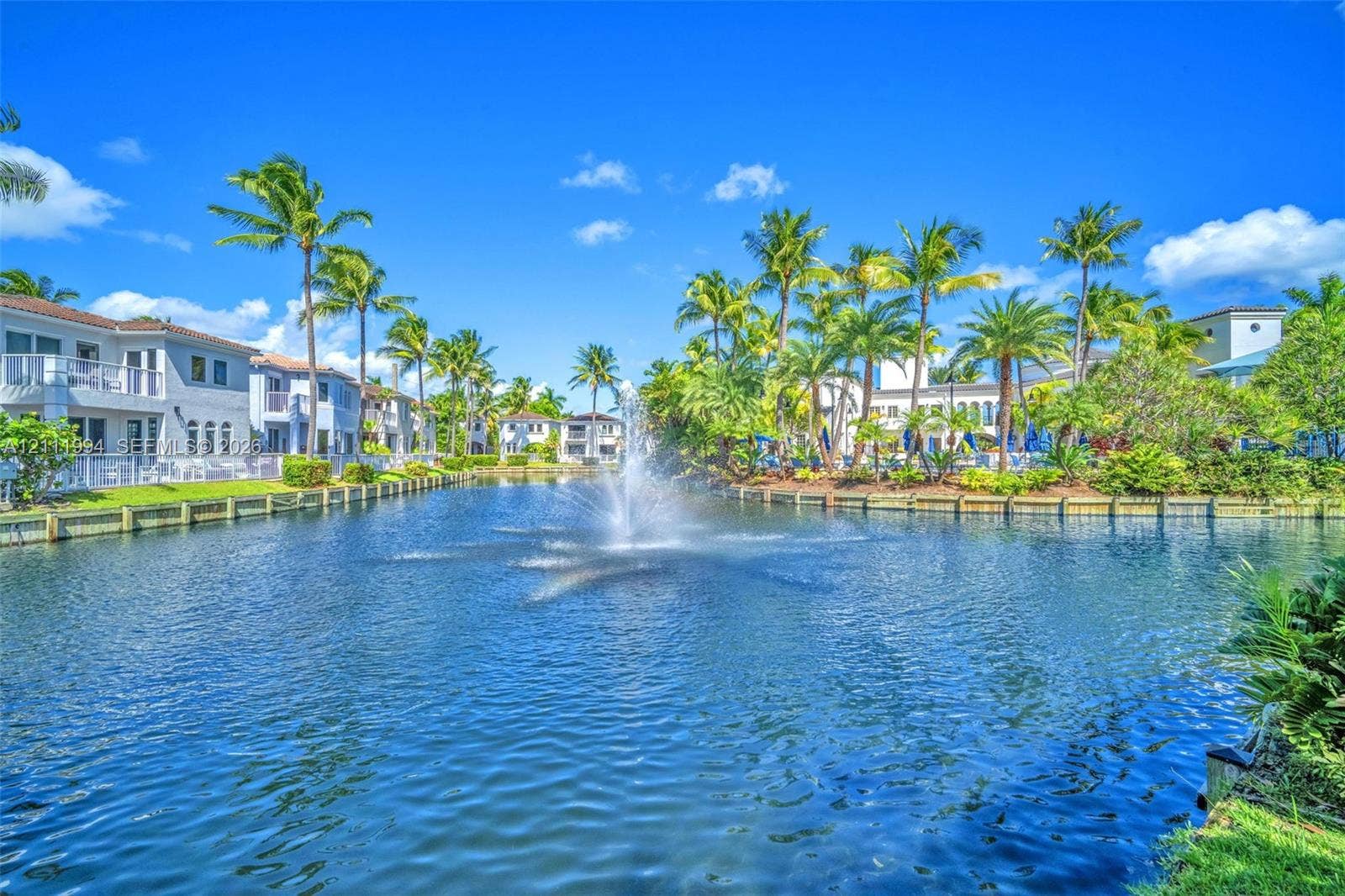 Manicured lakefront grounds featuring a central fountain, timber-framed bulkhead, and mature palm trees