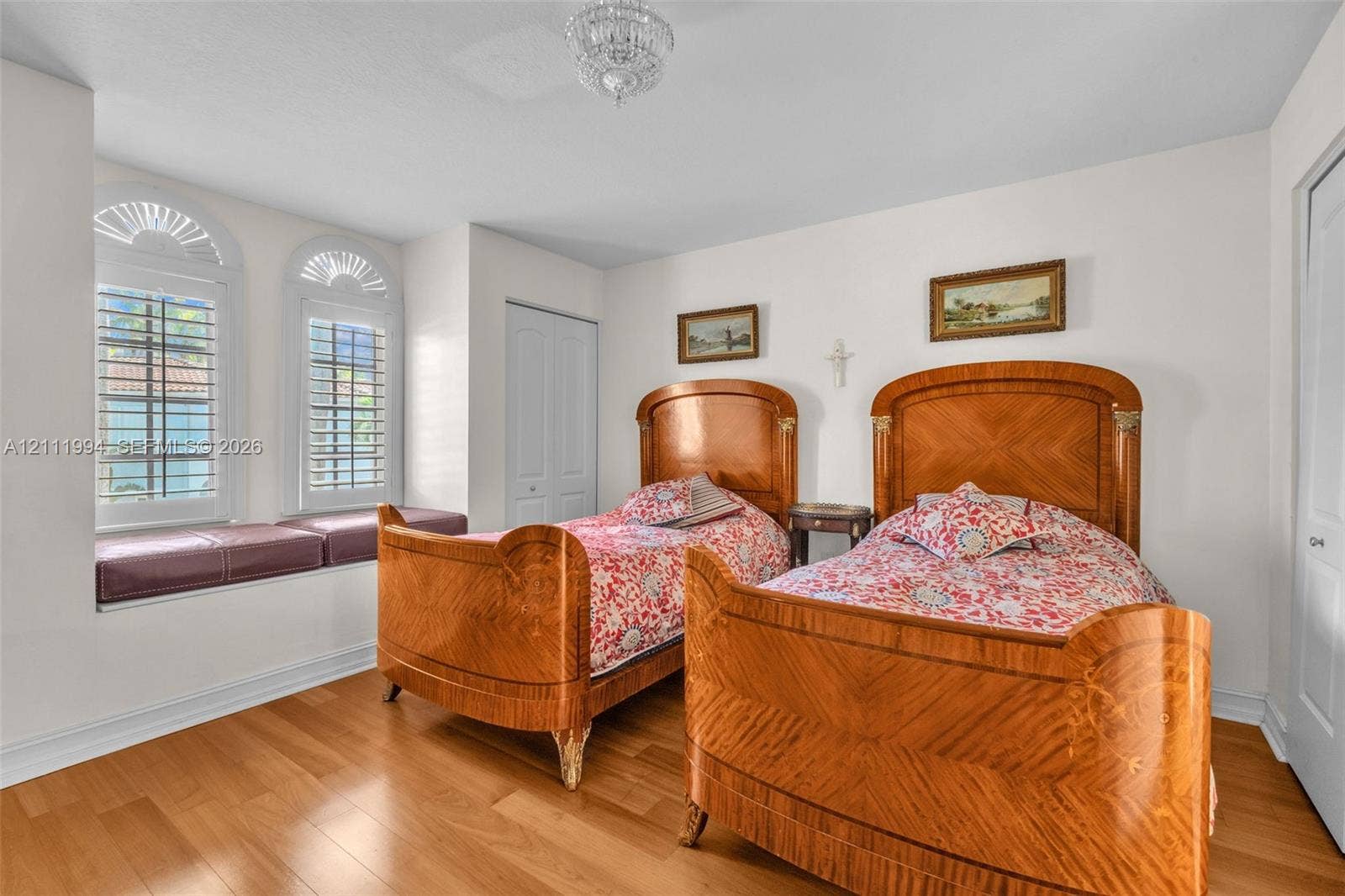 Wood-finish flooring, two arched windows with built-in window seating, and a crystal chandelier