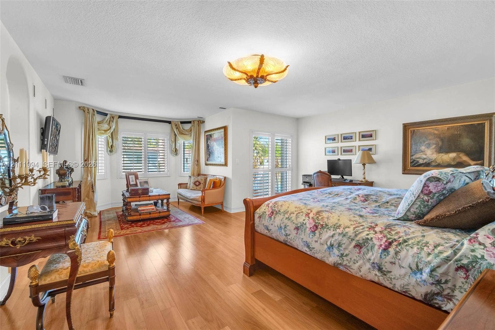 Wood-finish flooring, bay window with plantation shutters, arched wall niche, and glass-paneled double doors