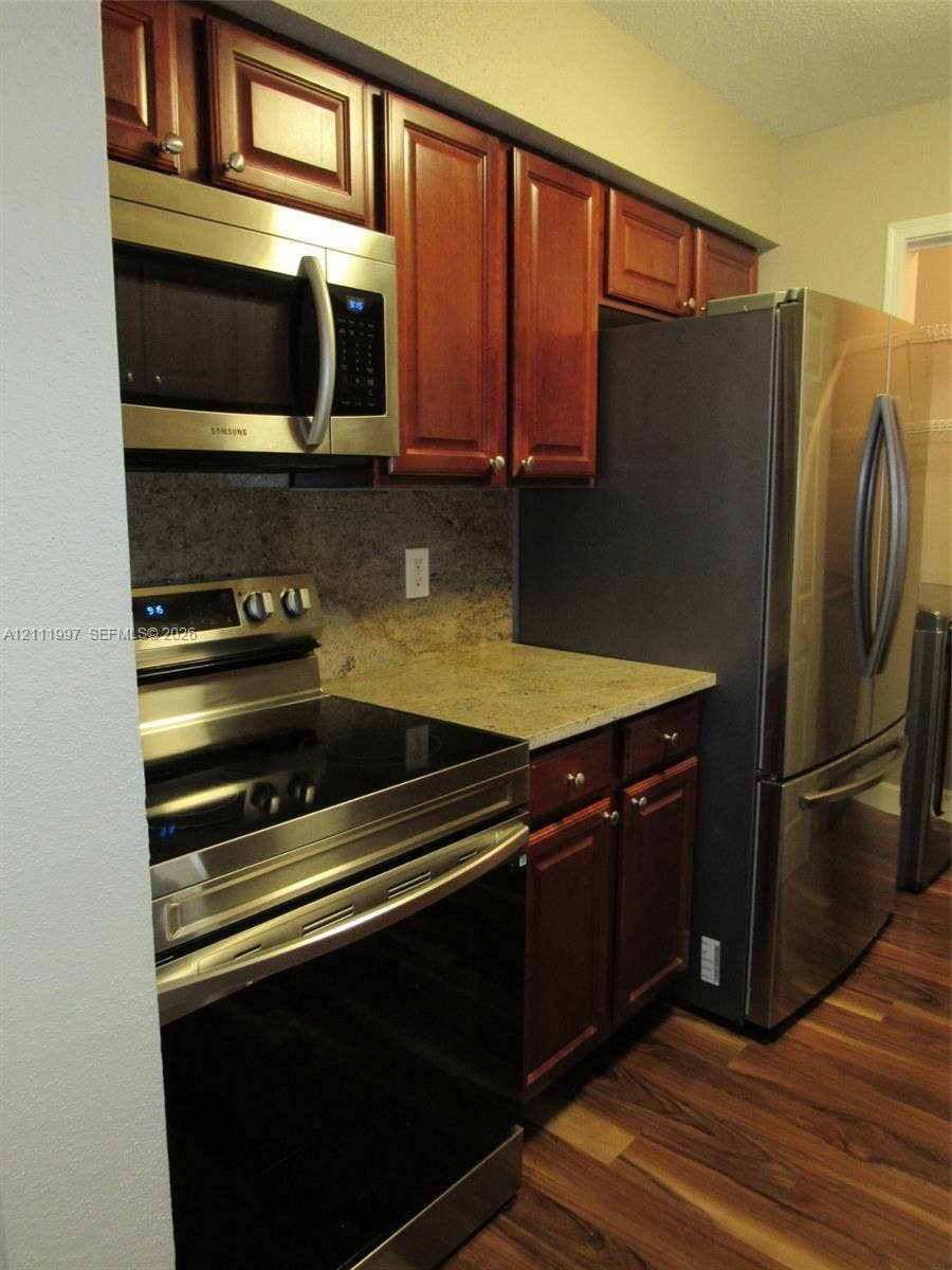 733 Riverside Drive, #1232, Coral Springs, Coral Springs, FL 33071 Kitchen featuring dark-toned wooden cabinetry, stone countertops, stainless steel appliances, and wood-finish flooring