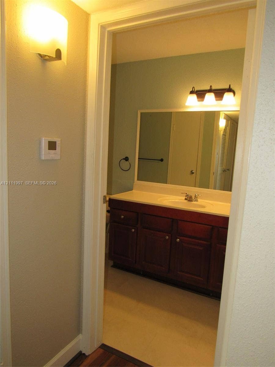 733 Riverside Drive, #1232, Coral Springs, Coral Springs, FL 33071 Vanity with dark wood-finish cabinetry, solid-surface countertop, integrated basin, wall-mounted three-light fixture, and large rectangular mirror