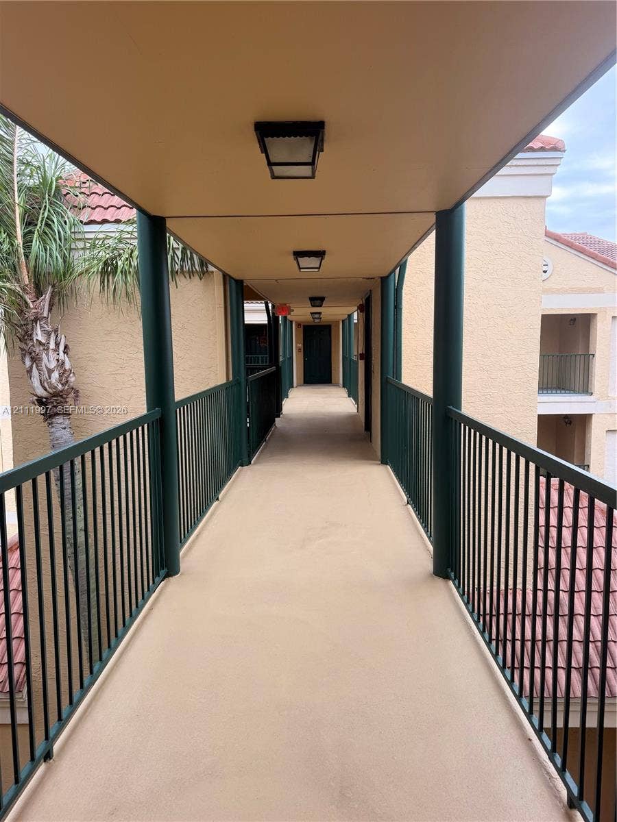 733 Riverside Drive, #1232, Coral Springs, Coral Springs, FL 33071 Covered exterior walkway featuring dark metal railings, neutral-tone stucco finishes, and flush-mount overhead lighting