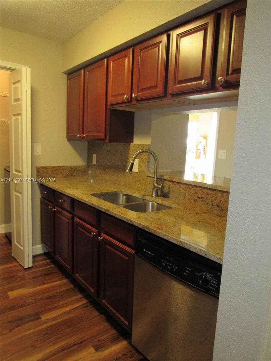 733 Riverside Drive, #1232, Coral Springs, Coral Springs, FL 33071 Rich-toned wood cabinetry, stone countertops, stainless steel dual-basin sink with arched faucet, stainless steel dishwasher, and wood-finish flooring