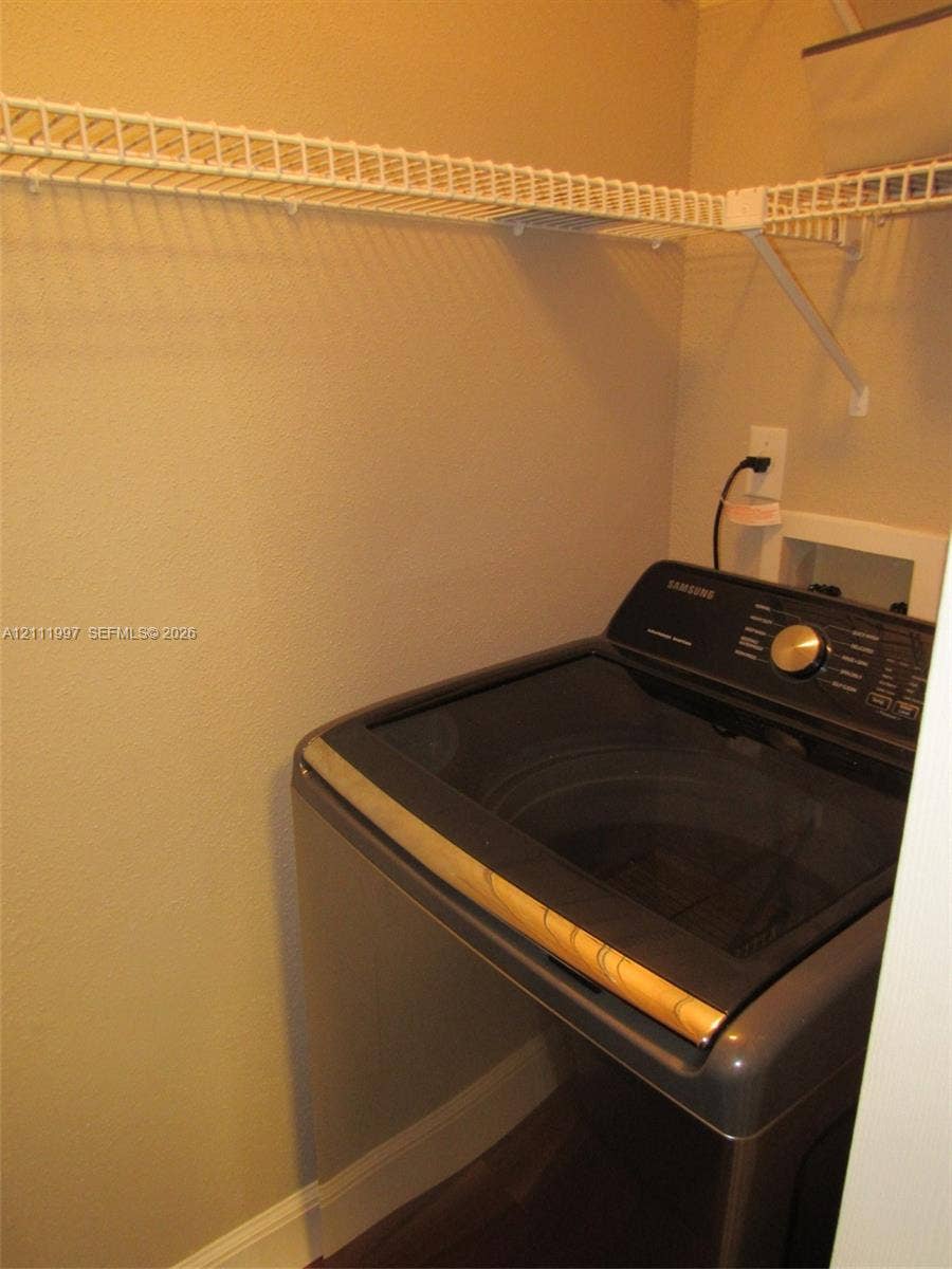 733 Riverside Drive, #1232, Coral Springs, Coral Springs, FL 33071 Laundry alcove featuring a top-load washer, wall-mounted electrical outlet, plumbing connection box, and overhead wire shelving