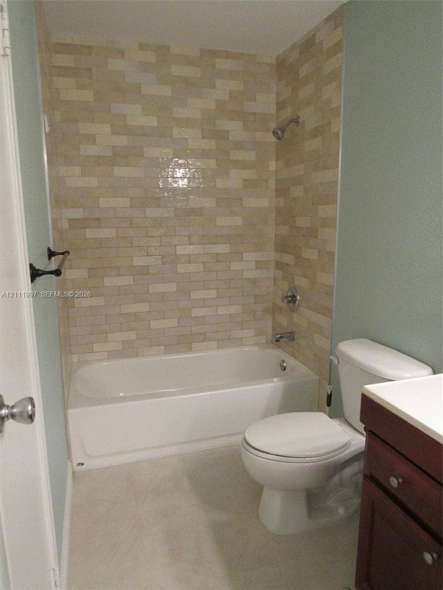 733 Riverside Drive, #1232, Coral Springs, Coral Springs, FL 33071 Bathroom featuring a tub-shower combination with multi-toned rectangular tile surround, a built-in dark wood vanity, and a high-profile toilet