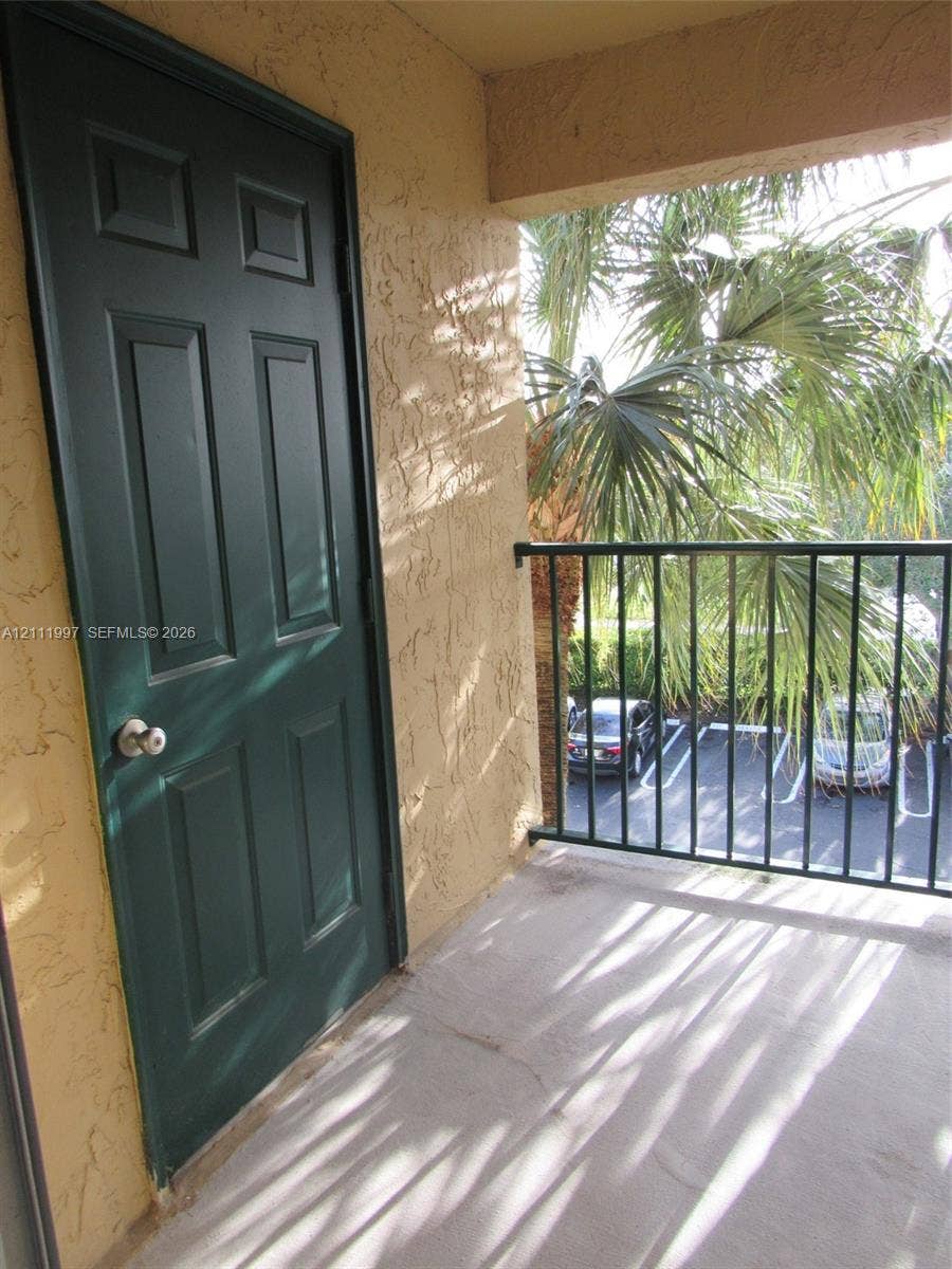 733 Riverside Drive, #1232, Coral Springs, Coral Springs, FL 33071 Exterior balcony featuring a smooth concrete floor, textured stucco walls, a six-panel door with a metallic hardware finish, and a black metal railing